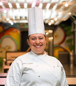 Woman smiling wearing chef coat and hat