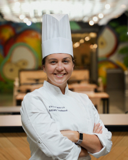 Woman smiling wearing chef coat and hat