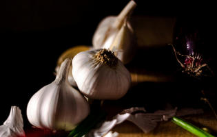 Garlic bulbs and loose cloves arranged on a wooden surface with green onion stalks