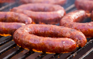 Close-up of grilled sausage links cooking over open flames on a barbecue grill.